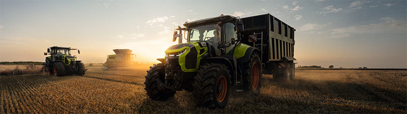 CLAAS ARION 8 -traktori vetää viljakärryä. Takana on toinen traktori ja CLAAS-leikkuupuimuri.