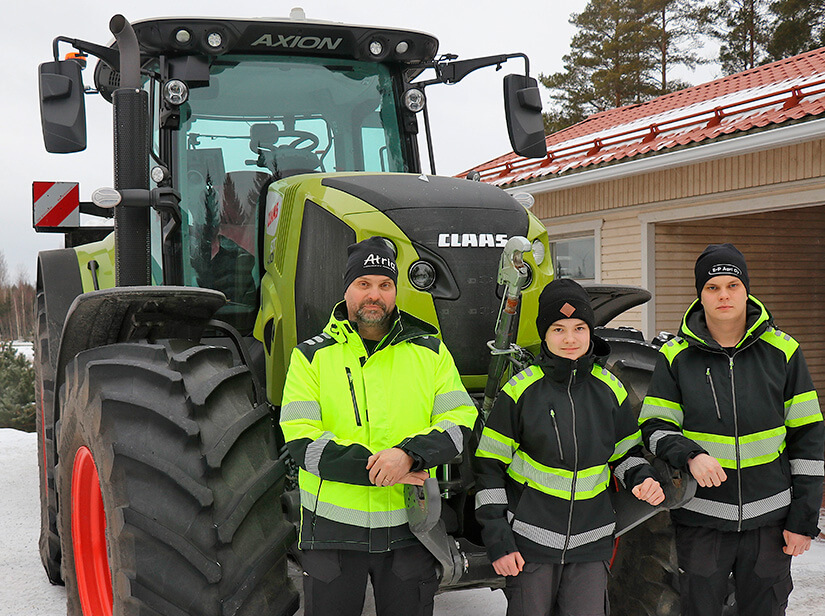 Koneurakoitsija Petri Peura seisoo poikiensa kanssa Claas-traktorin edessä.
