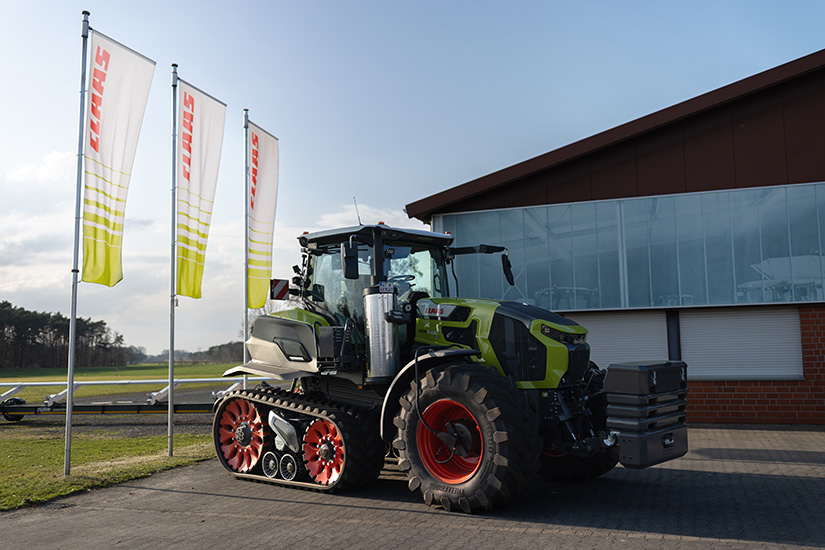 Claas Axion 9.450 -traktori teloilla seisoo Claas-lippujen edessä.