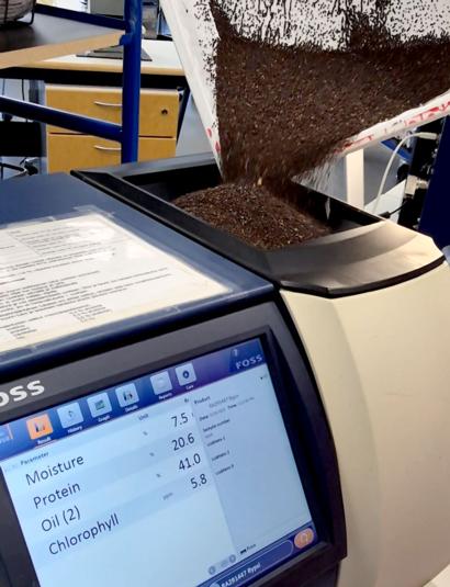 Tummaa näytettä kaadetaan laboratorion analysaattoriin, jonka näytöllä näkyvät mitatut ravintoarvot.