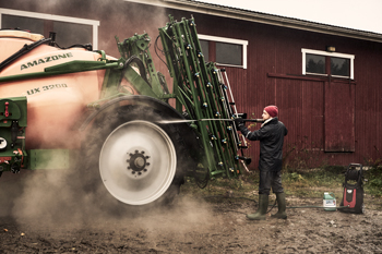 Mies ruiskuttaa painepesurilla Amazone-kylvökoneen rengasta