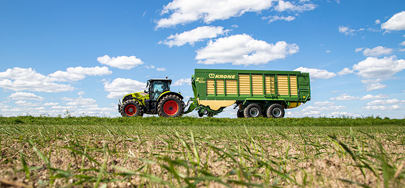 CLAAS vetää Kronen noukinvaunua keväisellä pellolla.