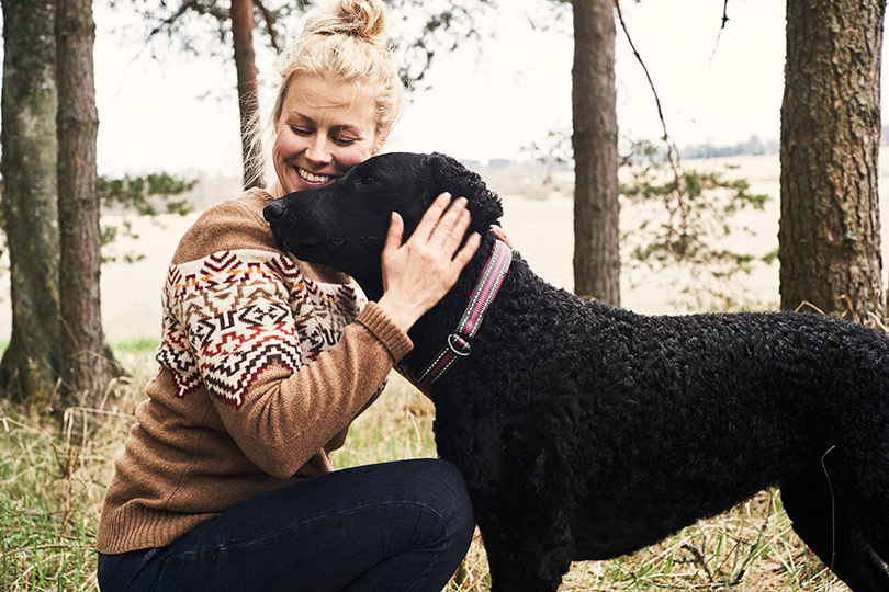 Vaaleatukkainen nainen halaa kiharaturkkista koiraa. Koiran turkki vaikuttaa terveeltä.
