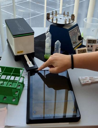 Henkilö käyttää tablettia näytteen mittaustulosten kirjaamiseen laboratoriossa.